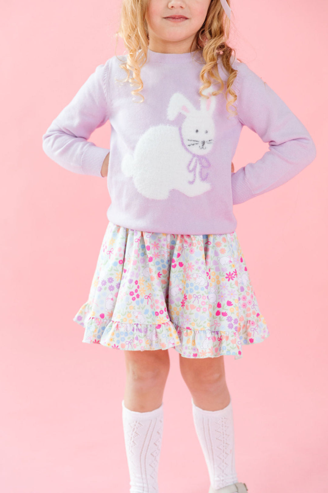 little girl in lavender knit sweater with white fluffy bunny design paired with Easter floral twirl dress and white pointelle knee high socks