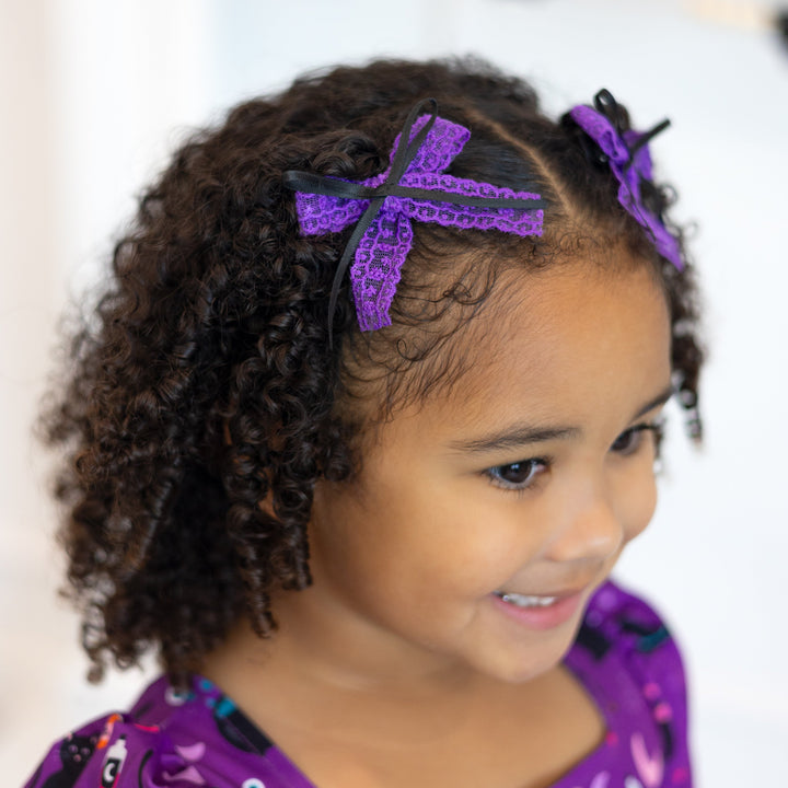 little girl in purple witchy print dress and matching purple lace pigtail bows with black ribbon trim
