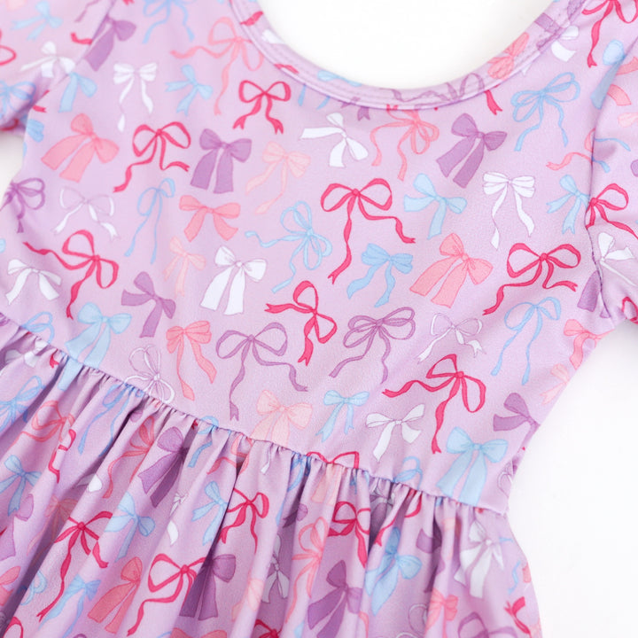 closeup of bow print twirl dress with pink, white, blue and purple bows on lavender