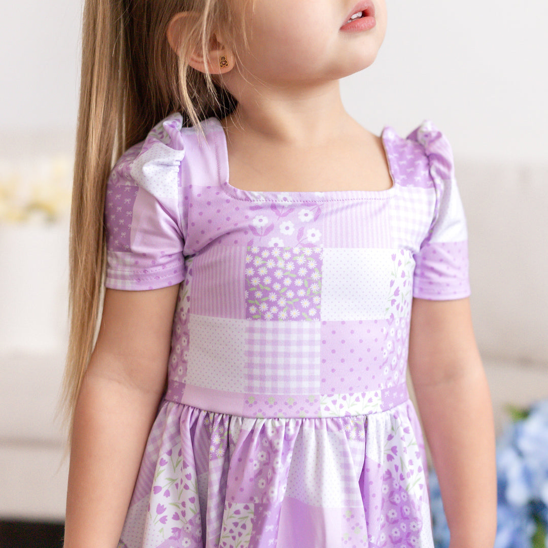 closeup of little girl wearing purple print square neck twirl dress with floral patchwork pattern for spring