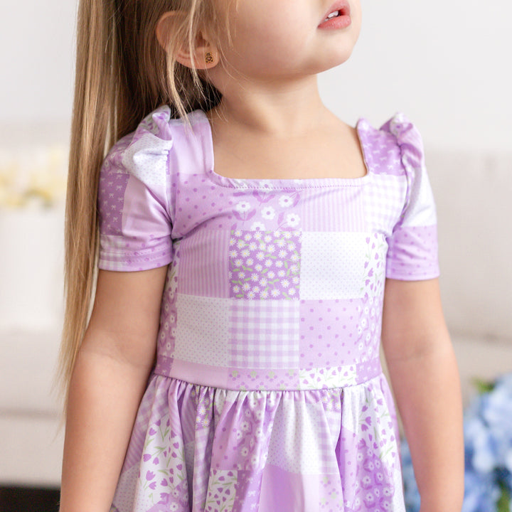 closeup of little girl wearing purple print square neck twirl dress with floral patchwork pattern for spring