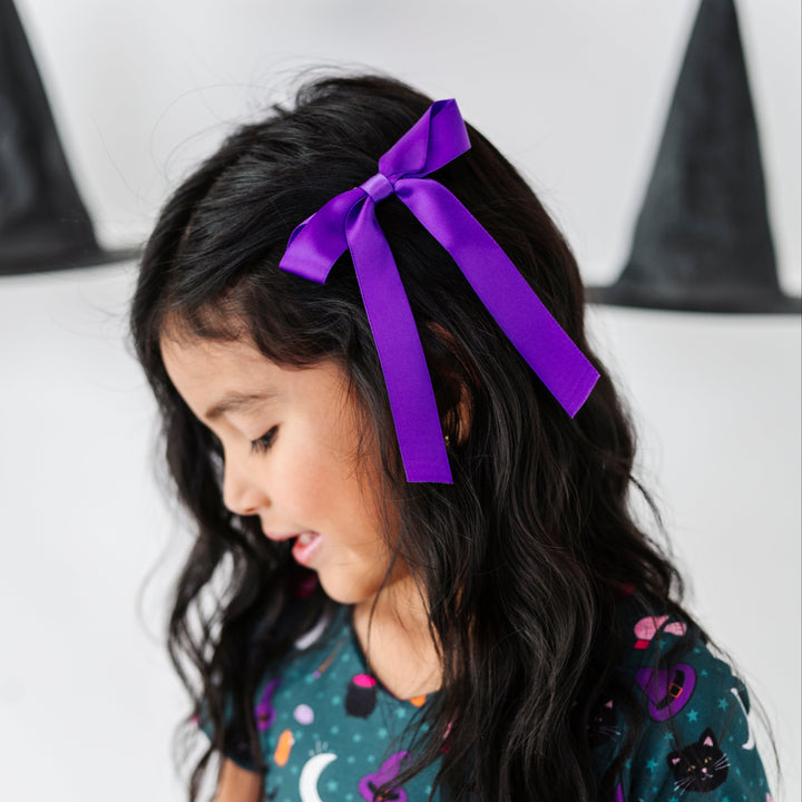 young girl in teal witch print twirl dress paired with matching bold purple satin ribbon hair bow on clip