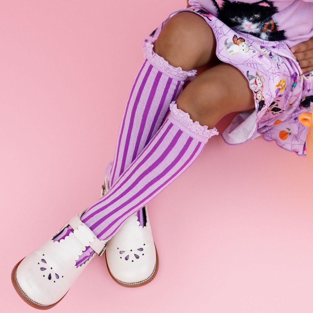 little girl wearing two tone purple striped knee socks with lace trim paired with white mary janes and kitten print twirl dress for Halloween