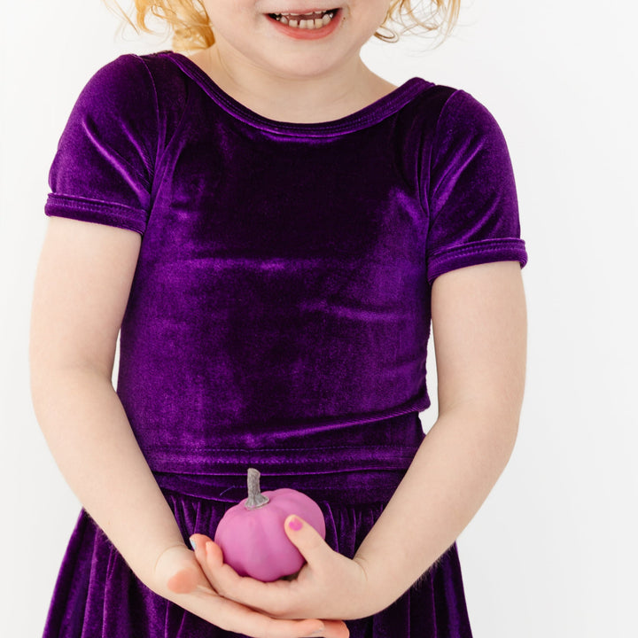 little girl holding lavender pumpkin in stretchy purple velvet short sleeve top and matching skort for Halloween