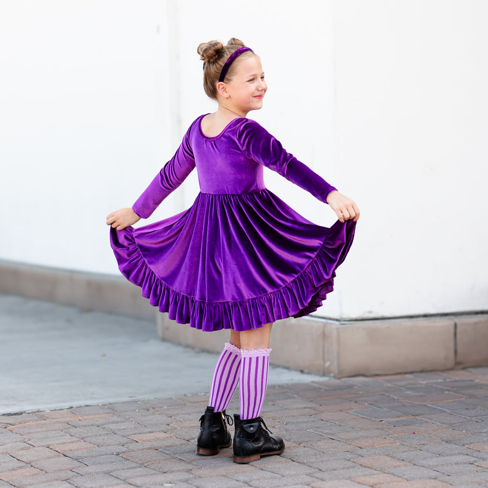 girl wearing purple velvet twirl dress with purple vertical stripe knee high socks