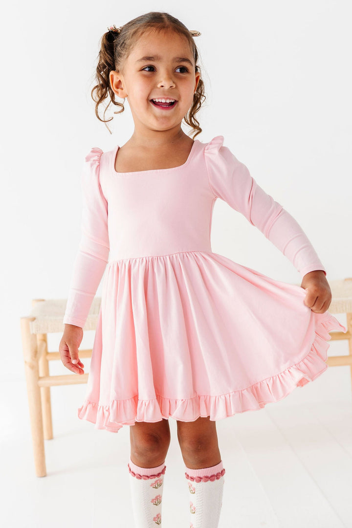 little girl wearing light pink twirl dress with long sleeves, square neckline and matching pink floral knee high socks