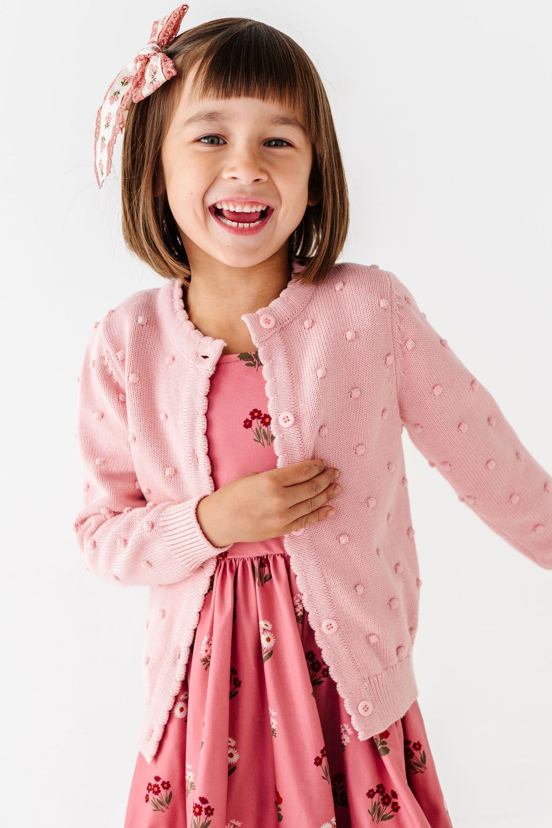 little girl wearing light pink bobble knit cardigan over pink floral fall dress
