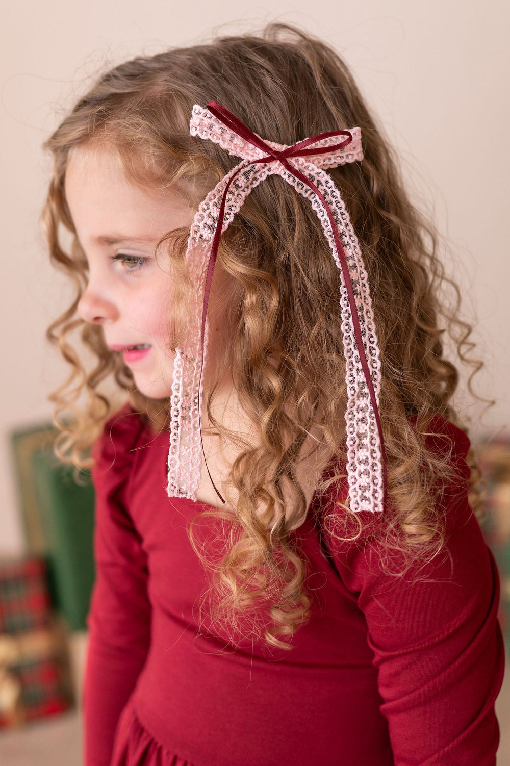 little girl with curly hair and pink and crimson red ribbon and lace hair bow in her hair. 