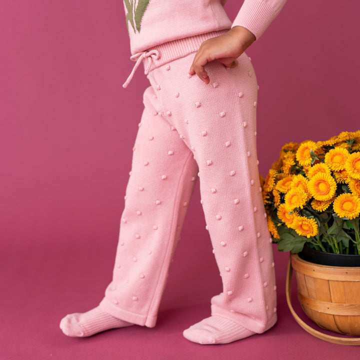little girl by yellow fall flowers in pink bubble textured knit sweater pants paired with matching pink sweater and socks
