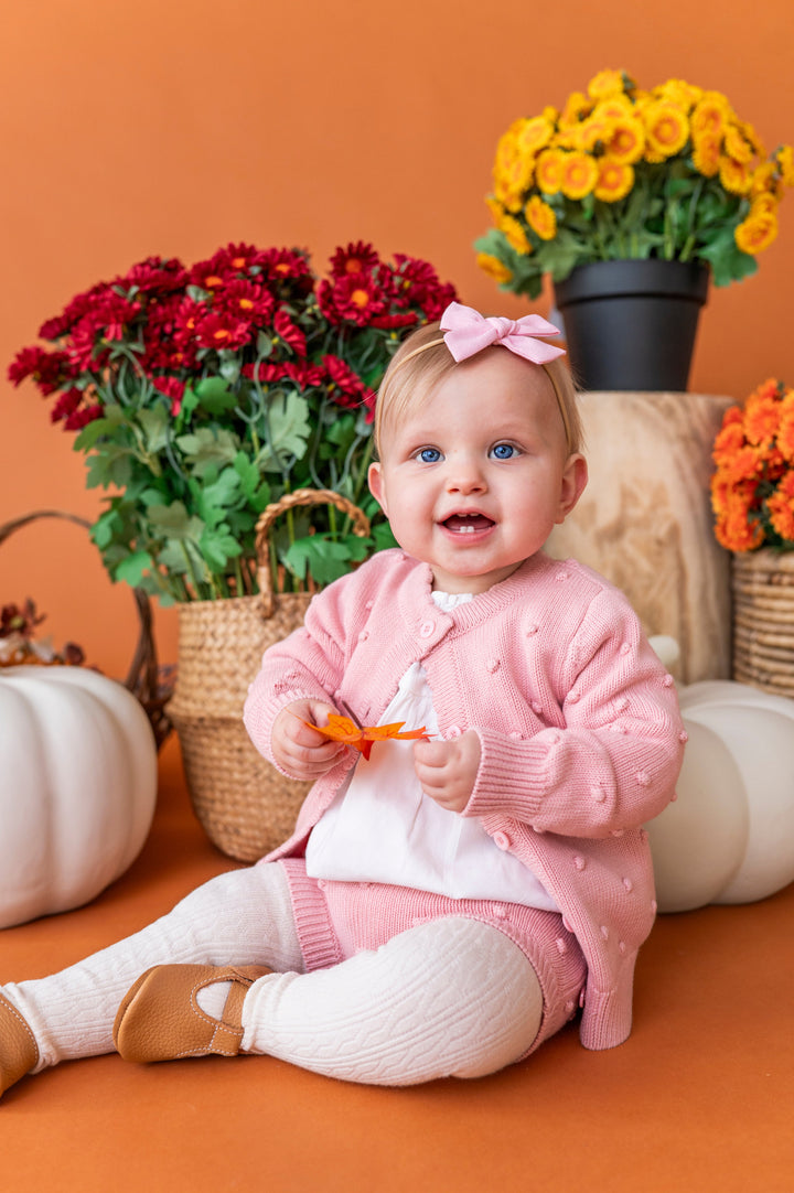 baby girl holding fall leaf in pink button front cardigan with bubble design paired matching bloomers and white cable knit tights