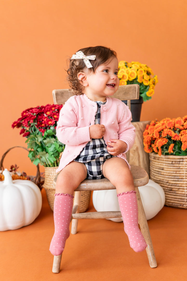 baby girl in buffalo plaid romper layered with light pink cotton knit button front cardigan with bubble design and matching pink knee socks