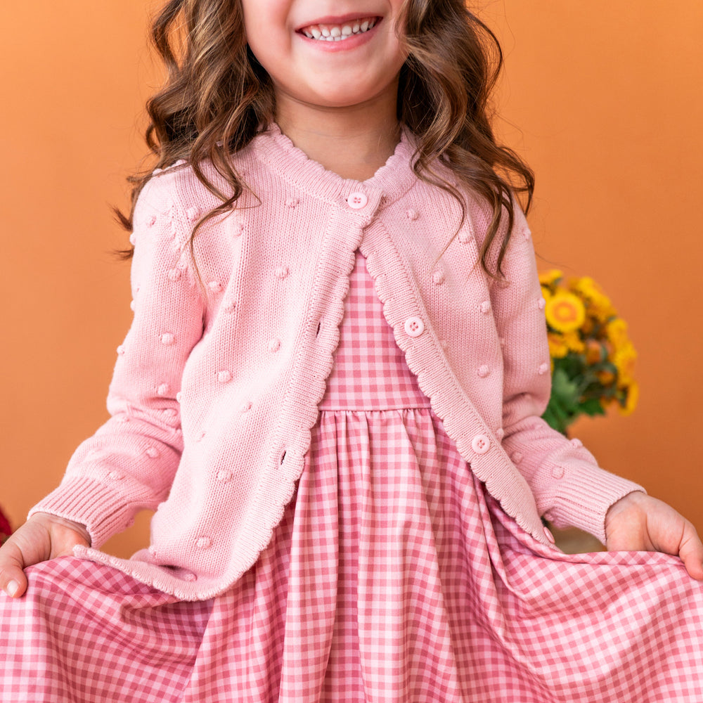 young girl in cotton knit bubble cardigan in light pink paired with matching pink gingham twirl dress