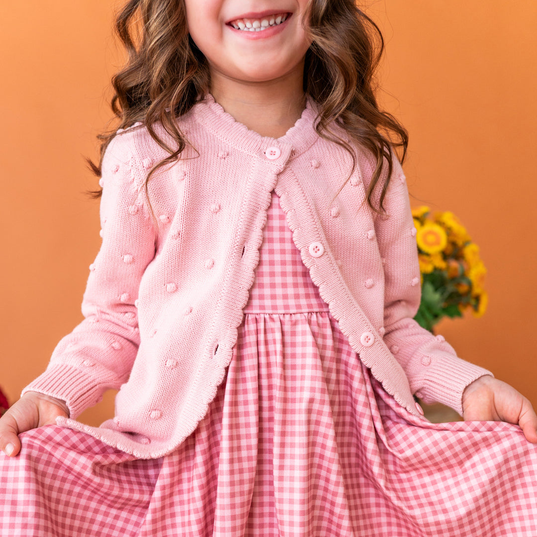 young girl in cotton knit bubble cardigan in light pink paired with matching pink gingham twirl dress
