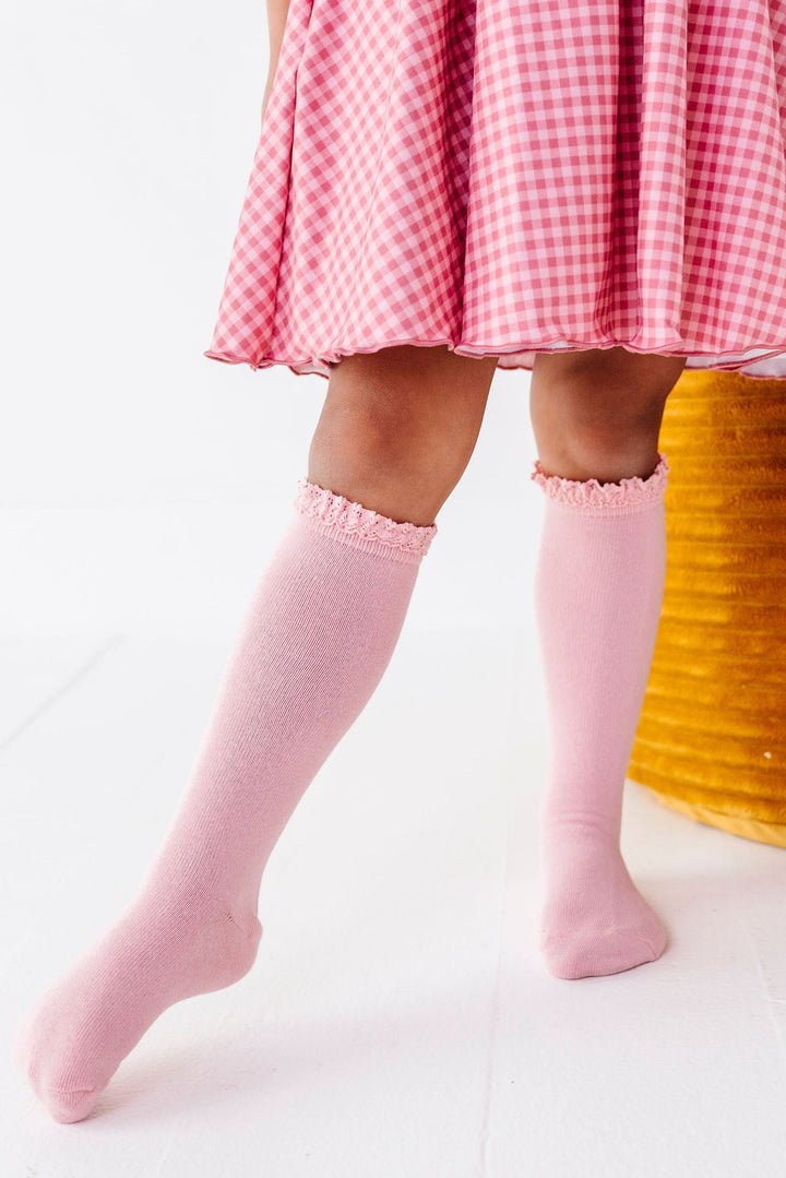 girl wearing quartz pink knee high socks with lace trim and matching pink gingham dress