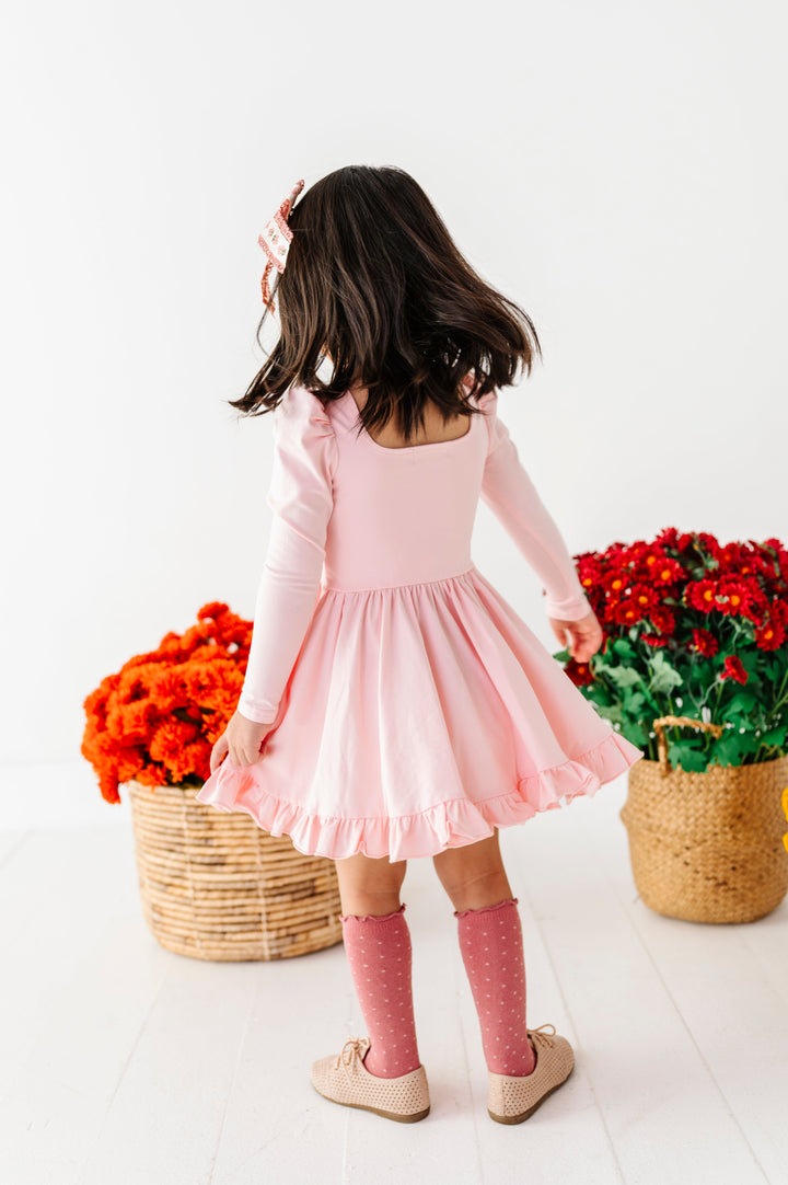 young girl twirling in front of baskets of fall flowers in pale pink long sleeve twirl dress, bright mauve dottie knee socks with matching floral hair bow