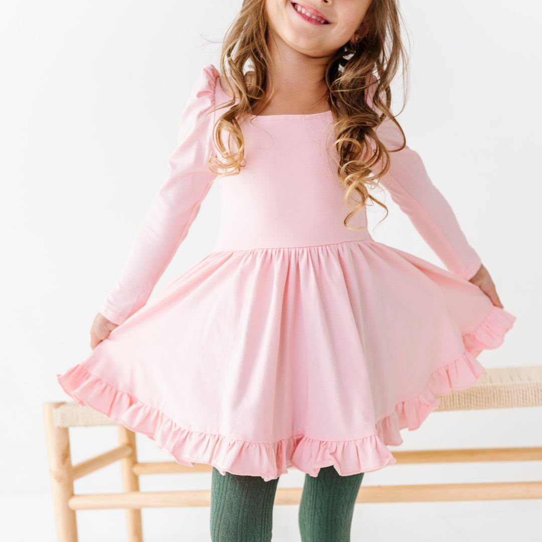 young girl in long sleeve light pink twirl dress with square neck design paired with sage green cable knit tights