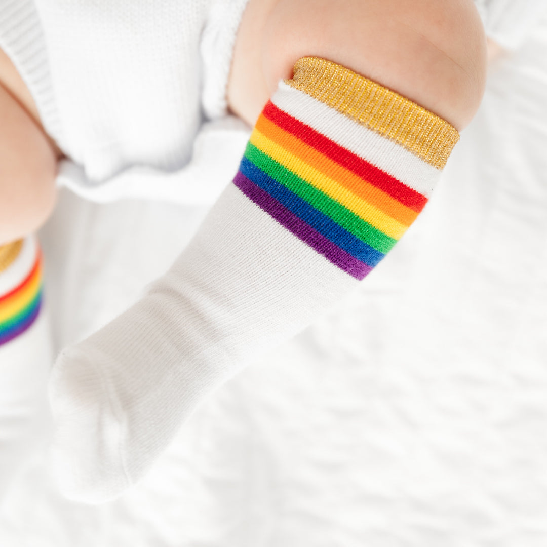 baby wearing white knee high sock with rainbow stripes and sparkly gold band