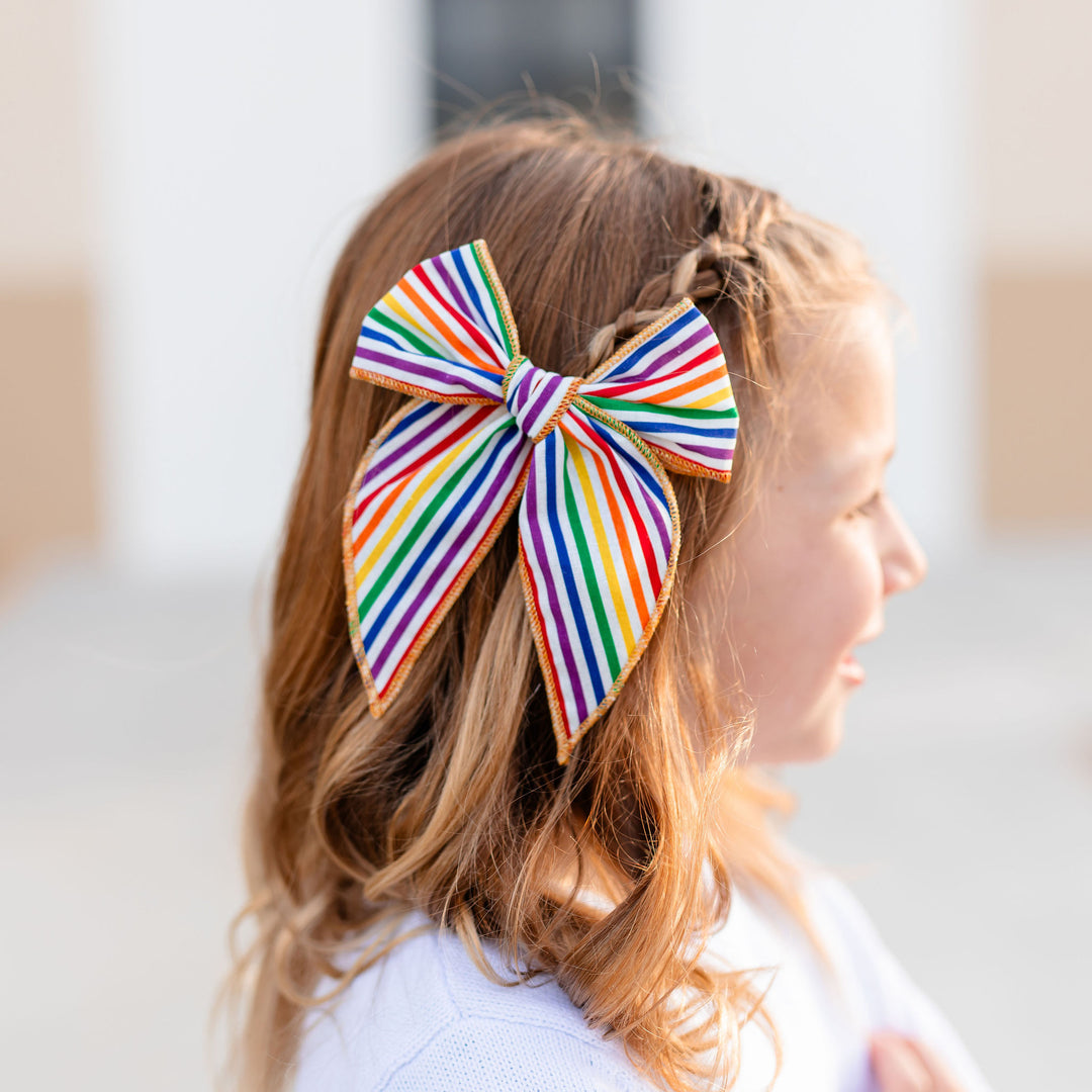 little girl wearing rainbow stripe hair bow with sparkly gold trim