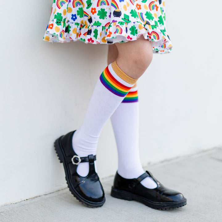 little girl wearing st. patrick's day dress with rainbow striped knee high socks with sparkly gold band and black patent leather shoes