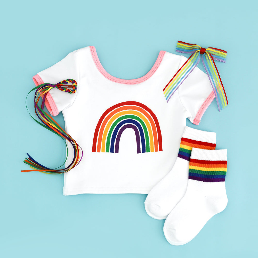 flat lay of white fitted tee with pink binding and rainbow design with matching rainbow socks and bow options for pride day