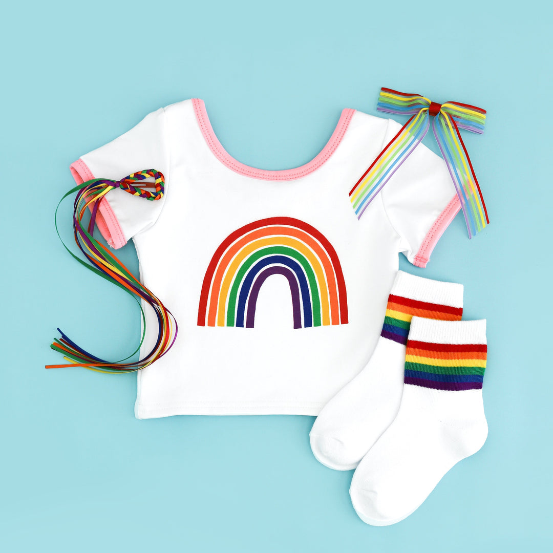 flat lay of white fitted tee with pink binding and rainbow design with matching rainbow socks and bow options for pride day