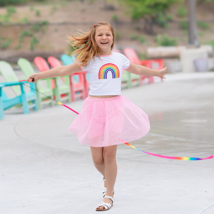 girl with rainbow ribbon twirling poolside in rainbow print tee and matching pink tutu shorts