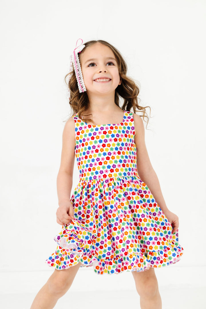 little girl in tank twirl dress with colorful daisies in a rainbow pattern and matching white lace hair bow with pink ribbon