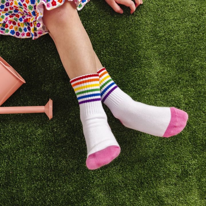 little girl sitting in grass with rainbow striped crew socks for pride month