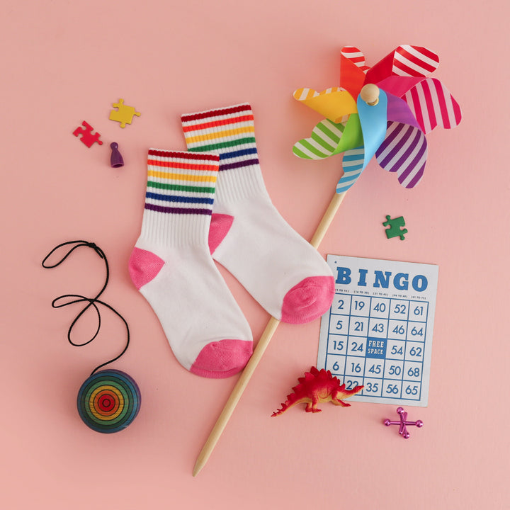 flat lay of white crew socks with pink heel and toe and rainbow stripes at the ankle styled for summer fun