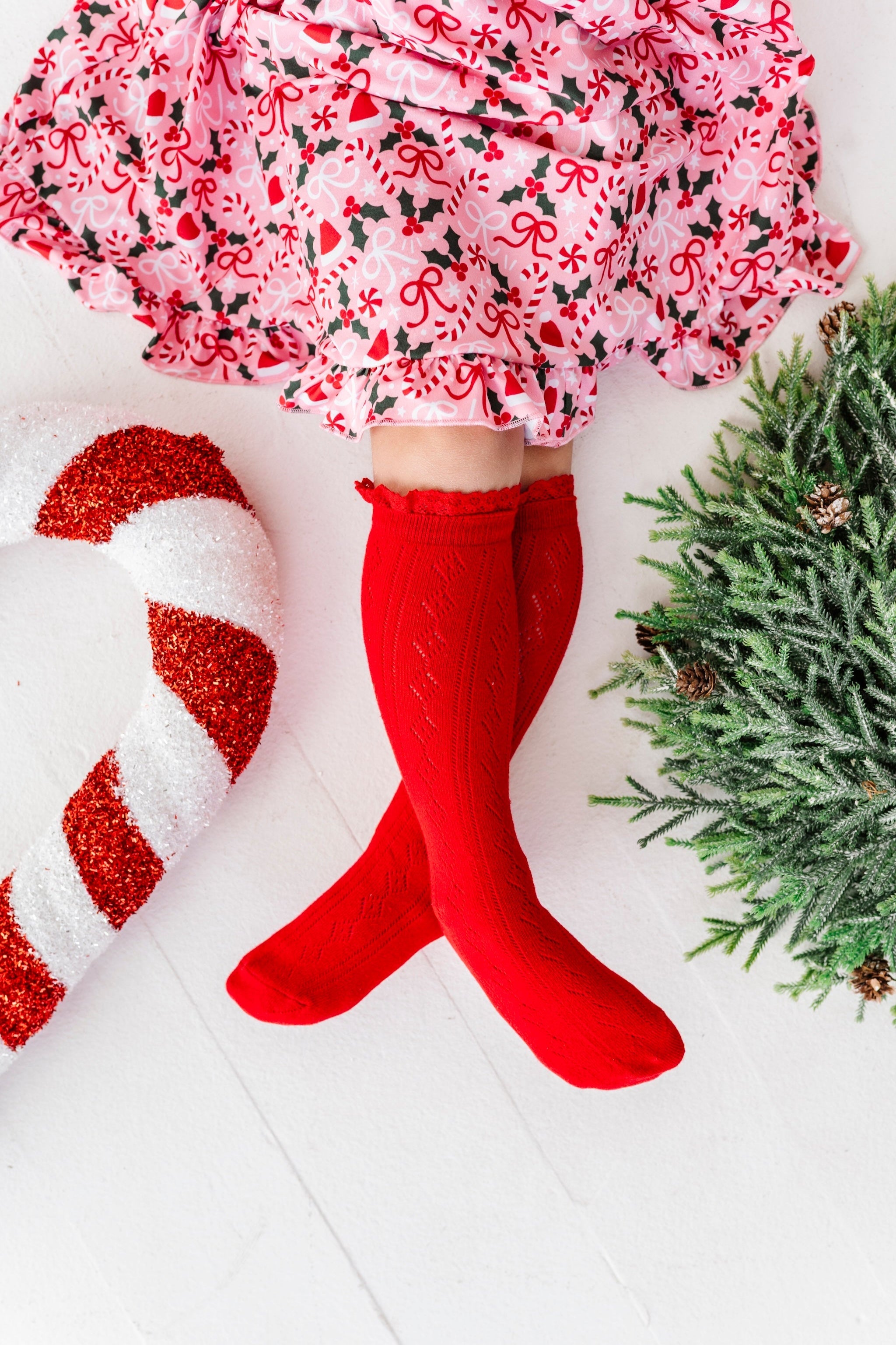 girl with christmas decorations in bright red pointelle knee socks with lace trim paired with peppermint and holly pink holiday twirl dress