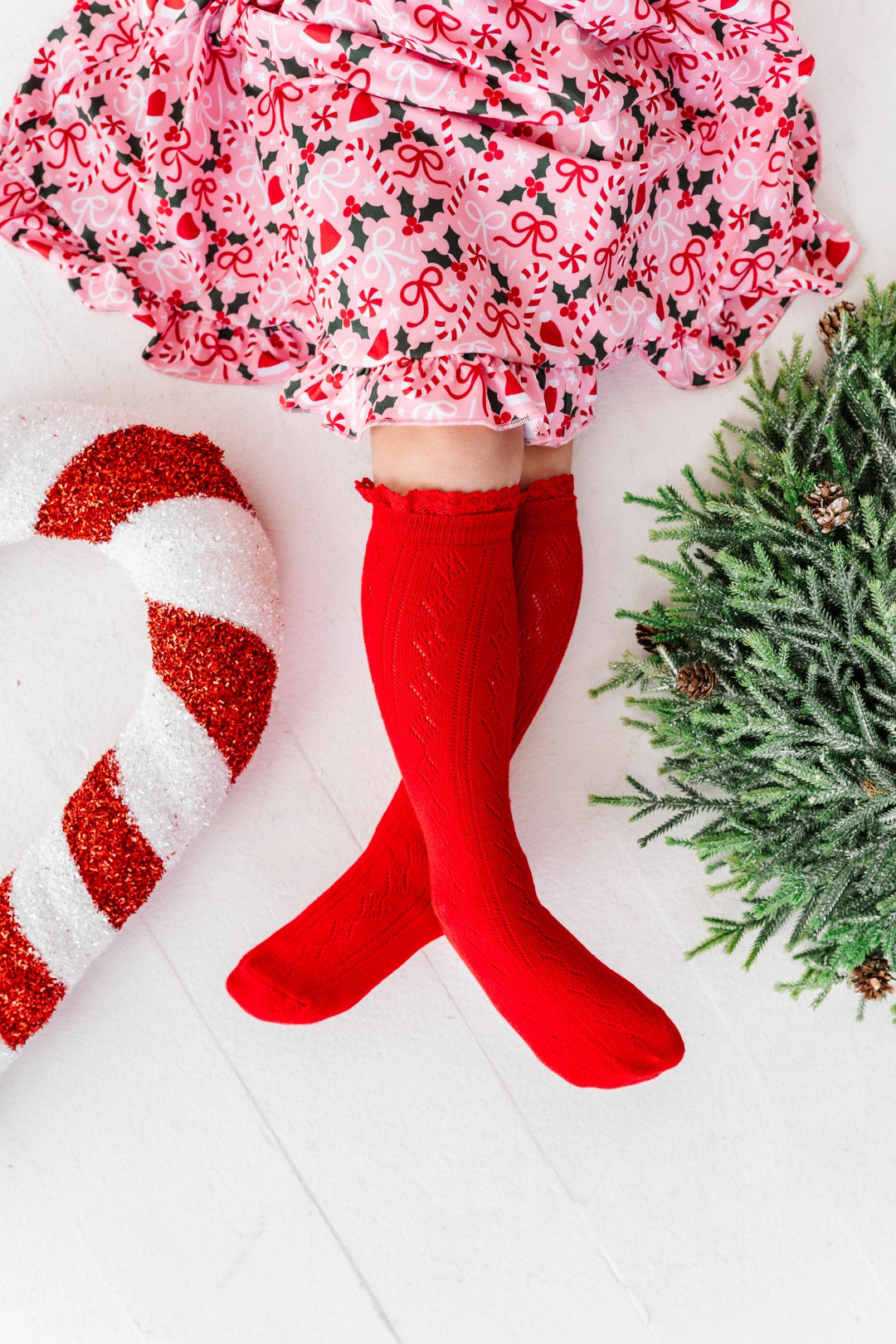 girl with christmas decorations in bright red pointelle knee socks with lace trim paired with peppermint and holly pink holiday twirl dress