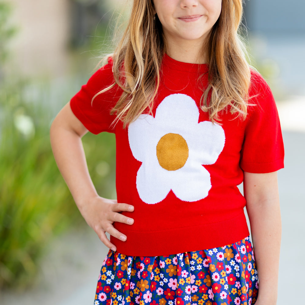 girl in short sleeve knit sweater in red with white flower on front and matching floral skort