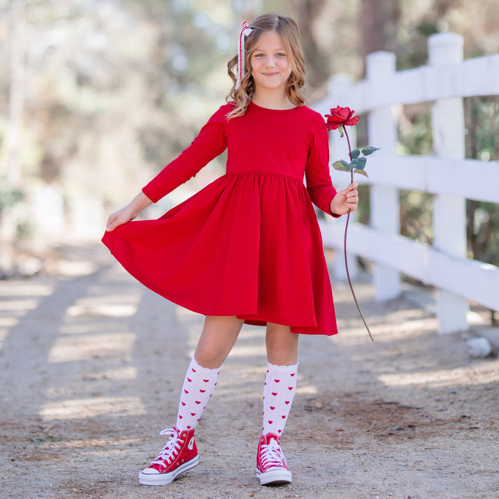 little girl holding rose in long sleeve red cotton twirl dress with matching red heart knee high socks and lace bow