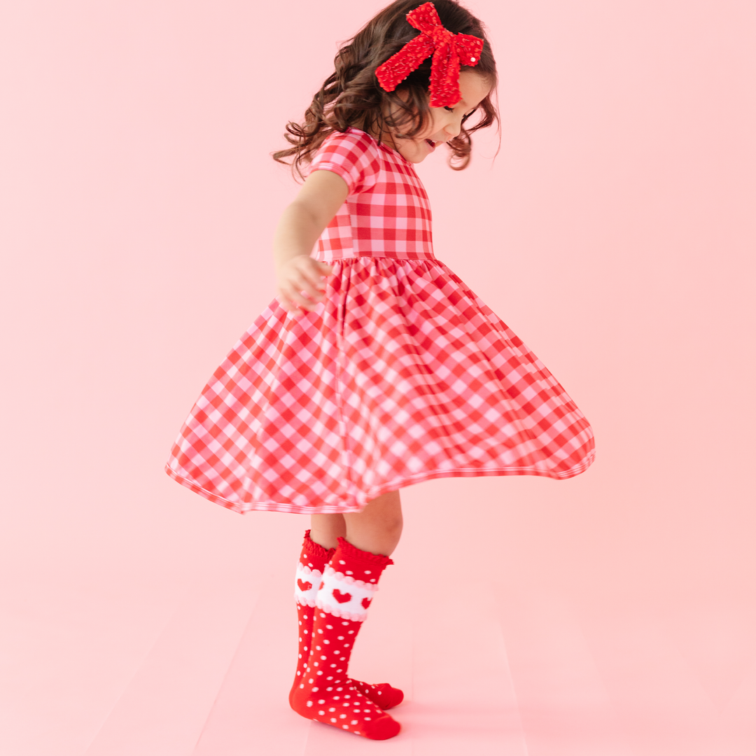 girl twirling in pink and red gingham scoop next dress and valentine's heart knee high socks