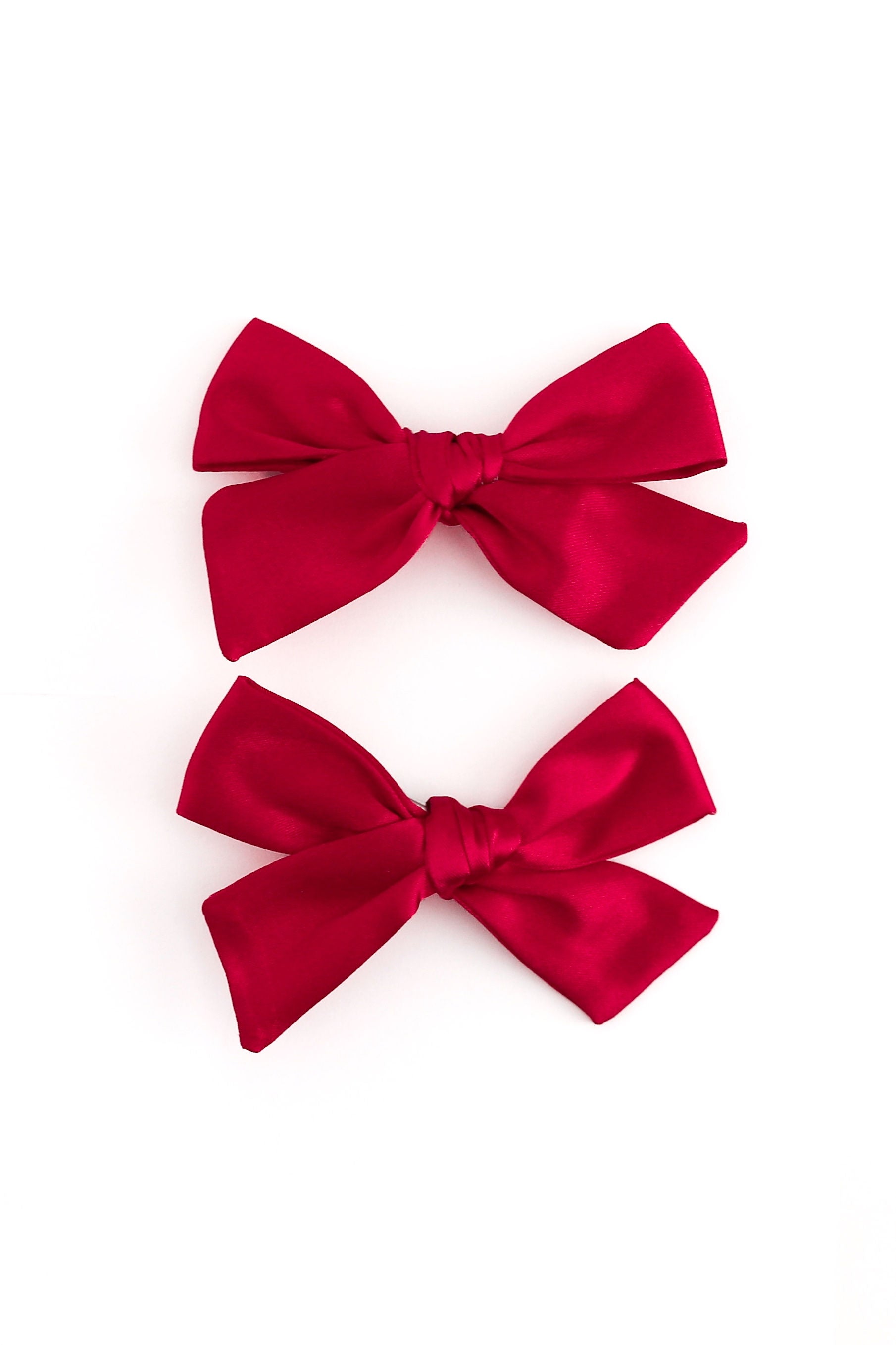 Two red satin bow hair clips arranged vertically on a plain white background.