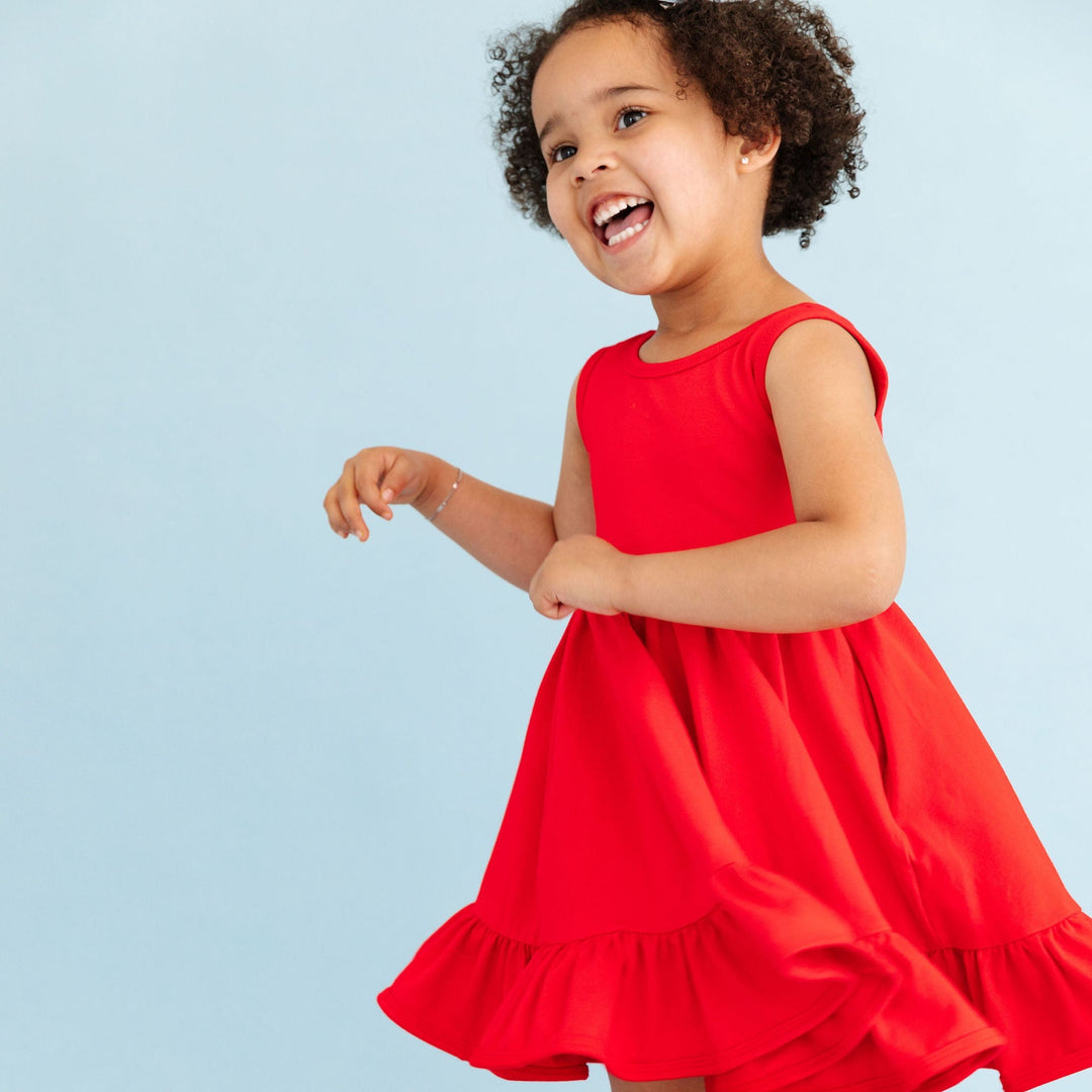 smiling little girl twirling in bright red cotton summer tank top dress
