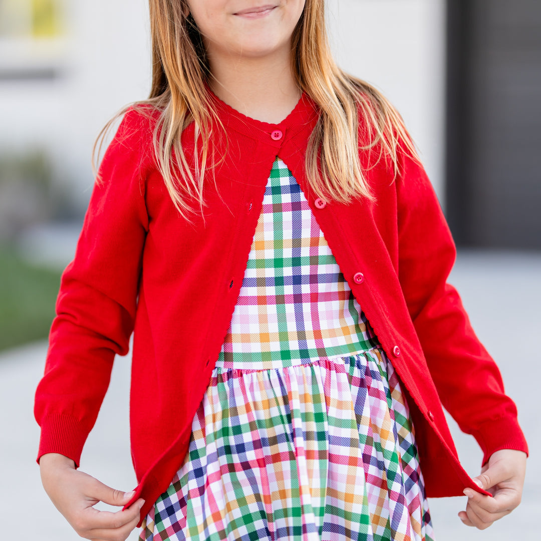 girl wearing back to school rainbow gingham twirl dress with matching red cotton button up cardigan with scallop trim