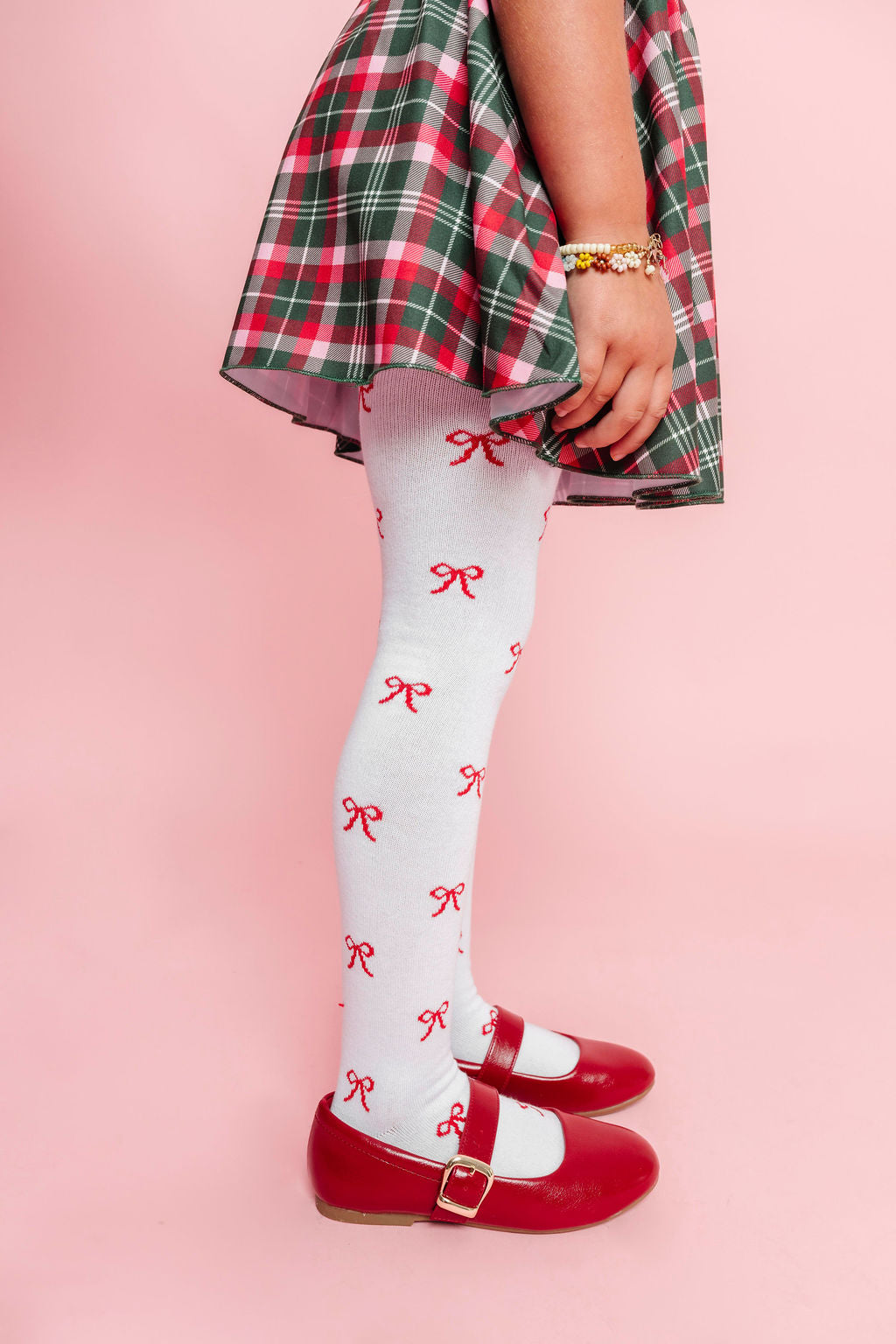closeup of little girl in white tights with red bow pattern paired with plaid skirt in classic Christmas colors and red mary janes