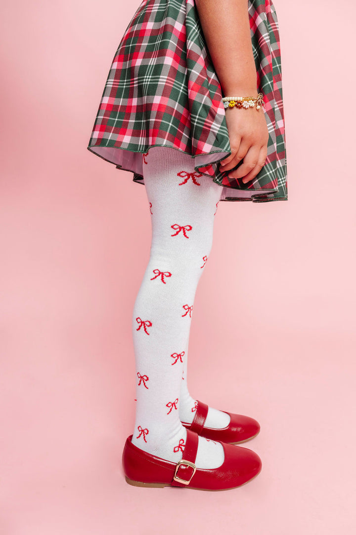 closeup of little girl in white tights with red bow pattern paired with plaid skirt in classic Christmas colors and red mary janes