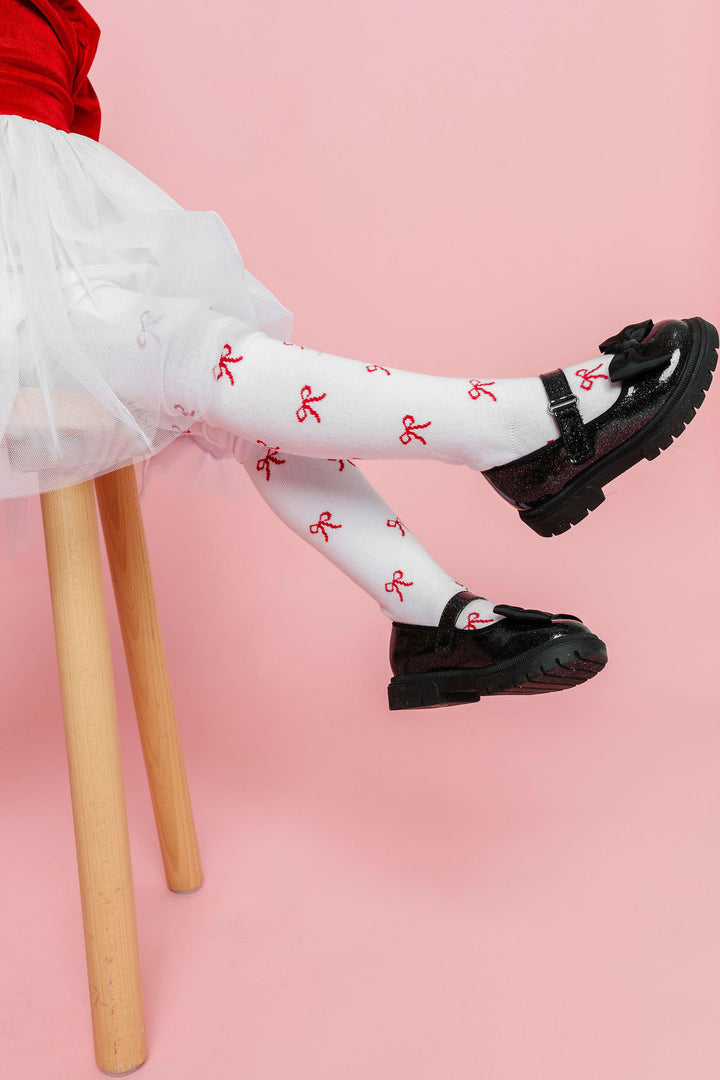 little girl wearing white Christmas tights with red bow design paired with red and white tutu dress and sparkly black mary janes