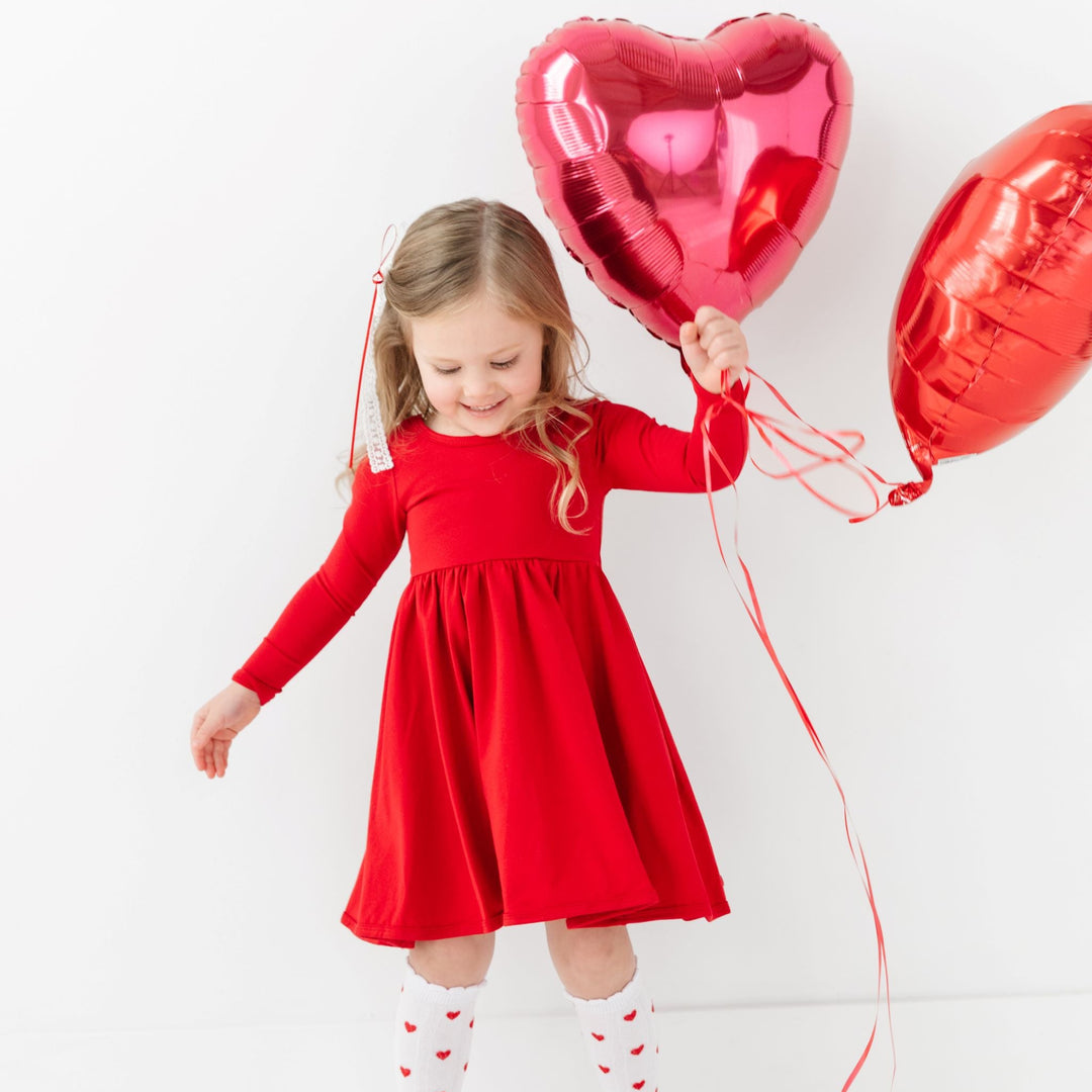 little girl holding heart balloons in long sleeve red cotton twirl dress with matching red heart knee high socks and lace bow