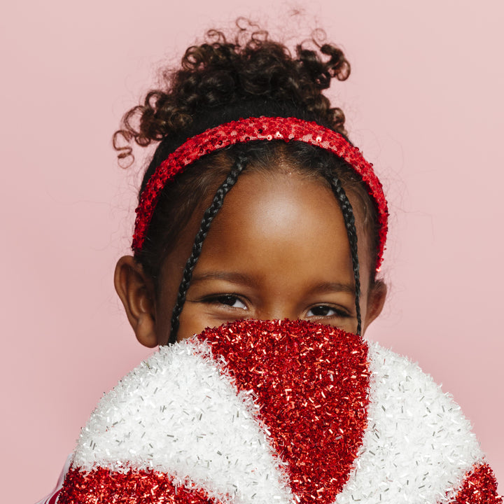 little girl holding sparkly candy cane decoration in sparkly red sequin headband