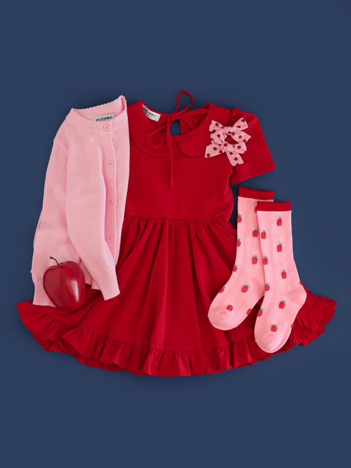 girl's apple themed flat lay for back to school and fall apple picking with bright red twirl dress, matching apple print socks, bows and pink cardigan