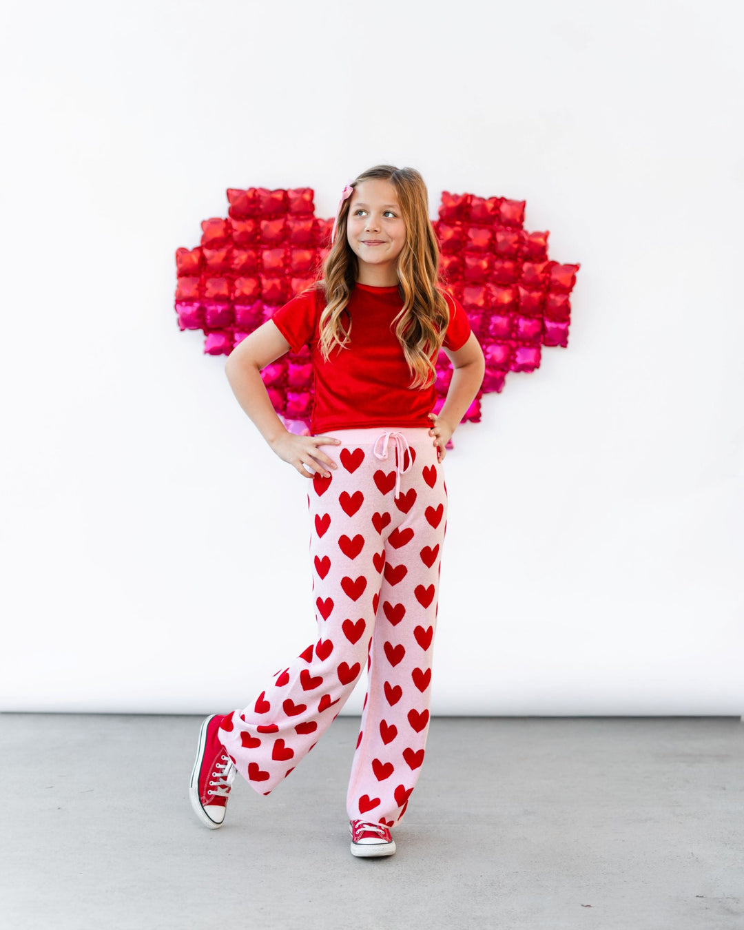 girl in front of heart shaped balloon wearing bright red velvet top paired with light pink and red heart sweater pants and red sneakers for Valentine's day