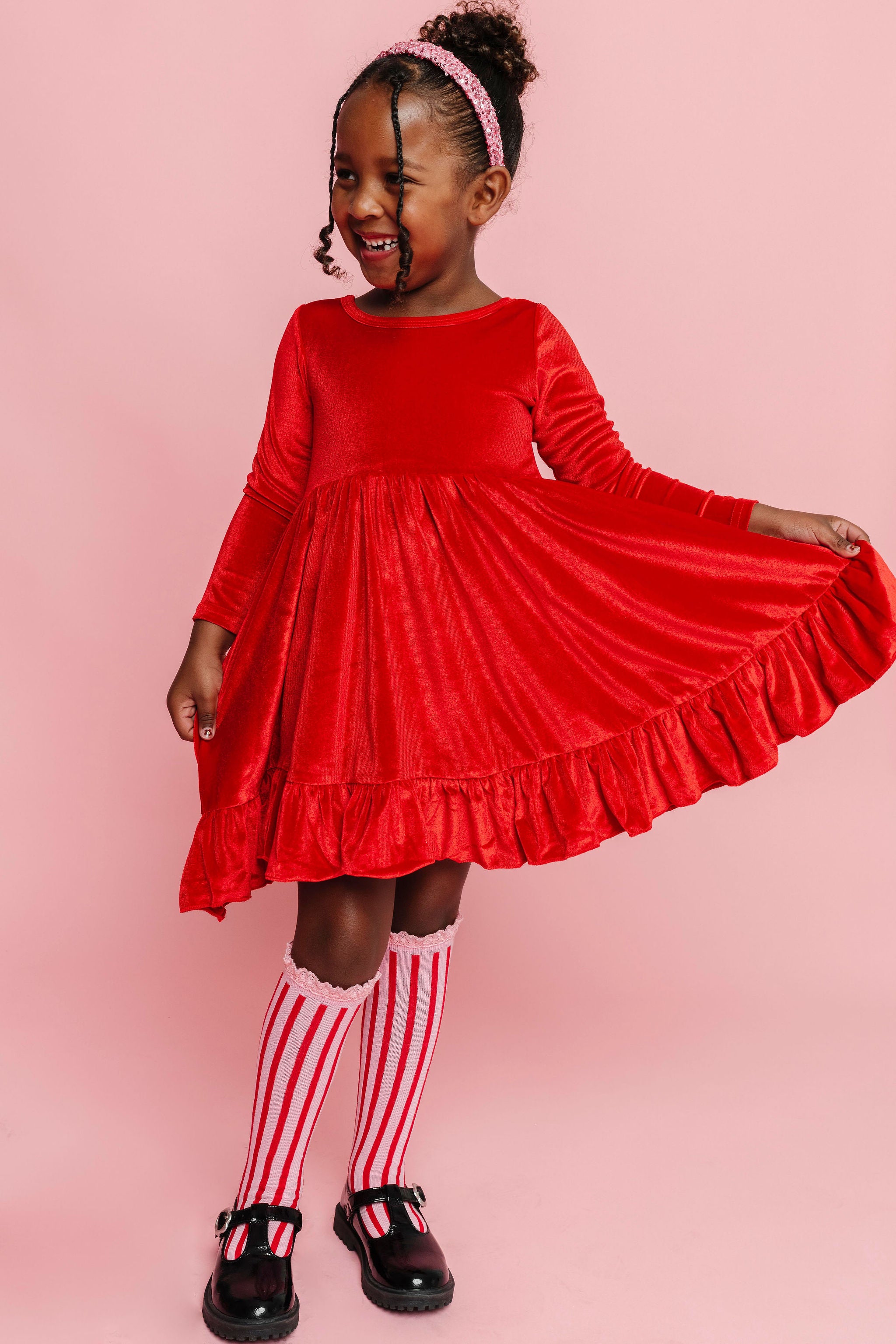 little girl in bright Christmas red velvet dress, pink and red striped knee socks and sparkly pink sequin headband