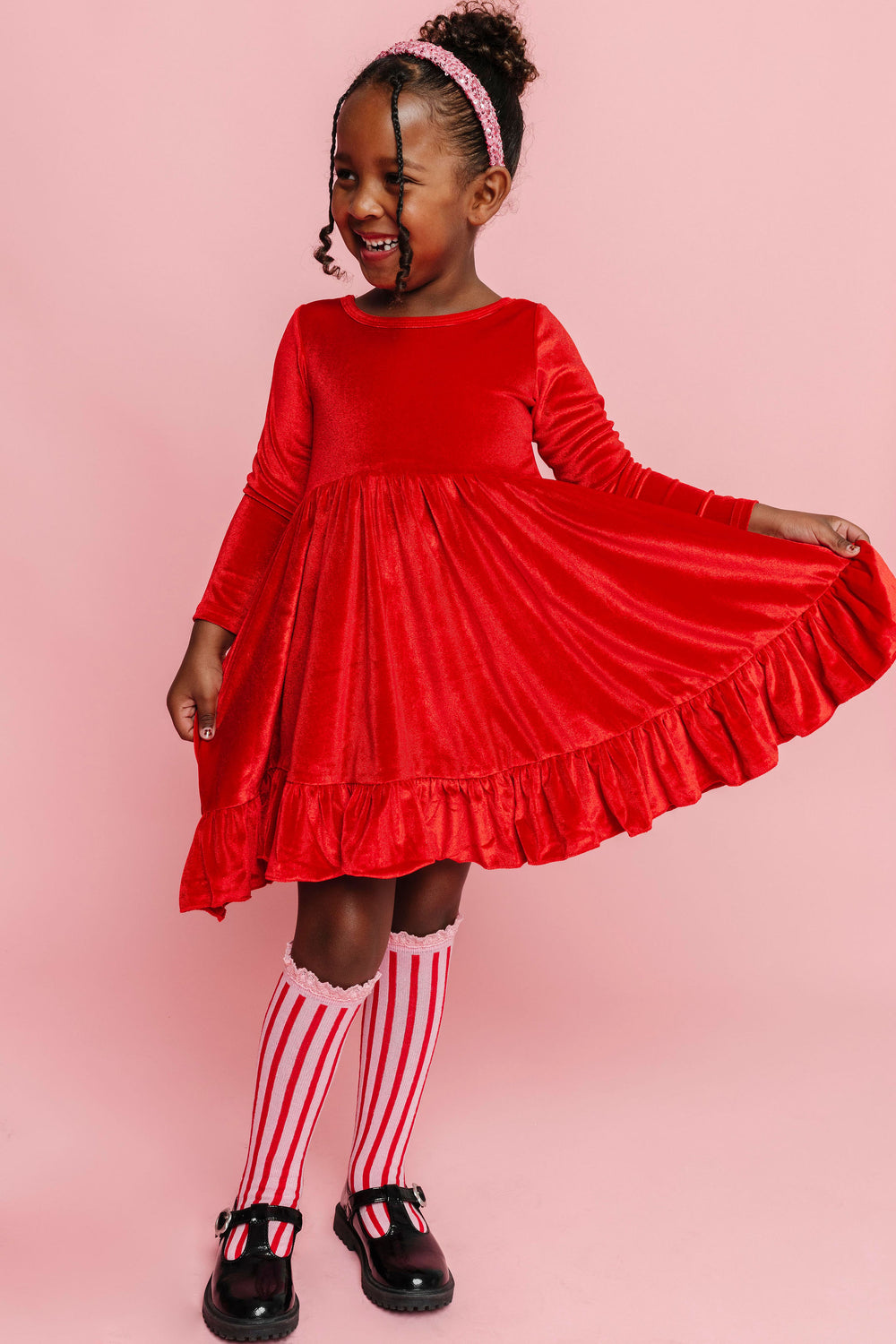 little girl in bright Christmas red velvet dress, pink and red striped knee socks and sparkly pink sequin headband