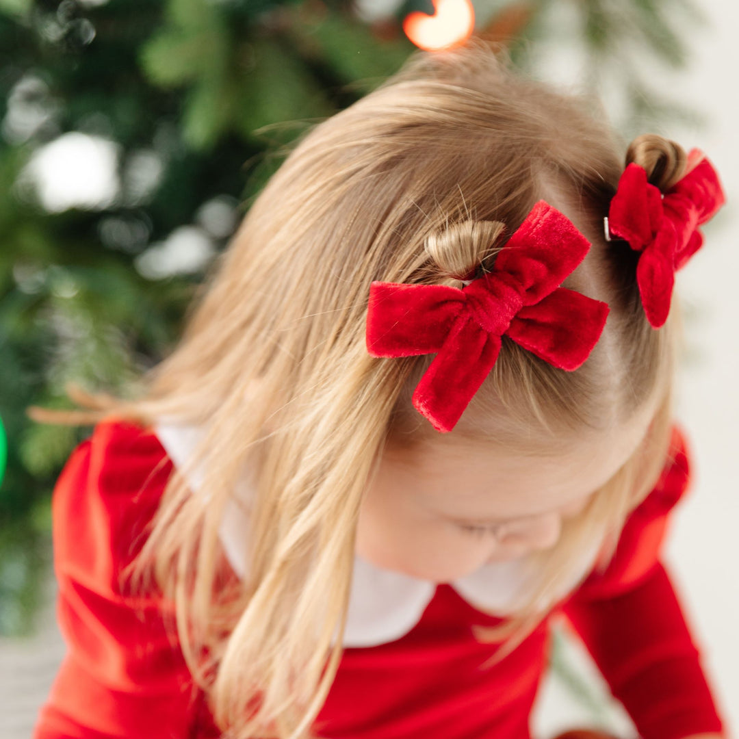 little girl in Santa inspired velvet dress with matching red velvet Christmas pigtail bows