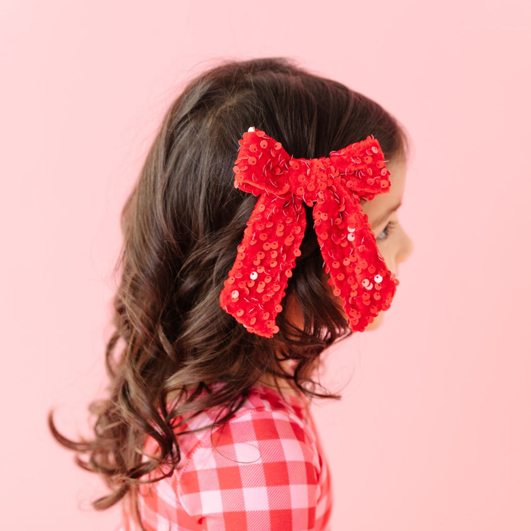 little girl in red velvet and sequin Valentine's Day bow and matching red and pink gingham twirl dress