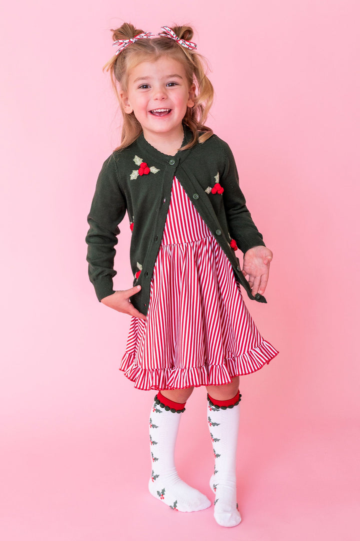 little girl wearing christmas themed outfit with red candystripe dress and holly cardigan and knee highs