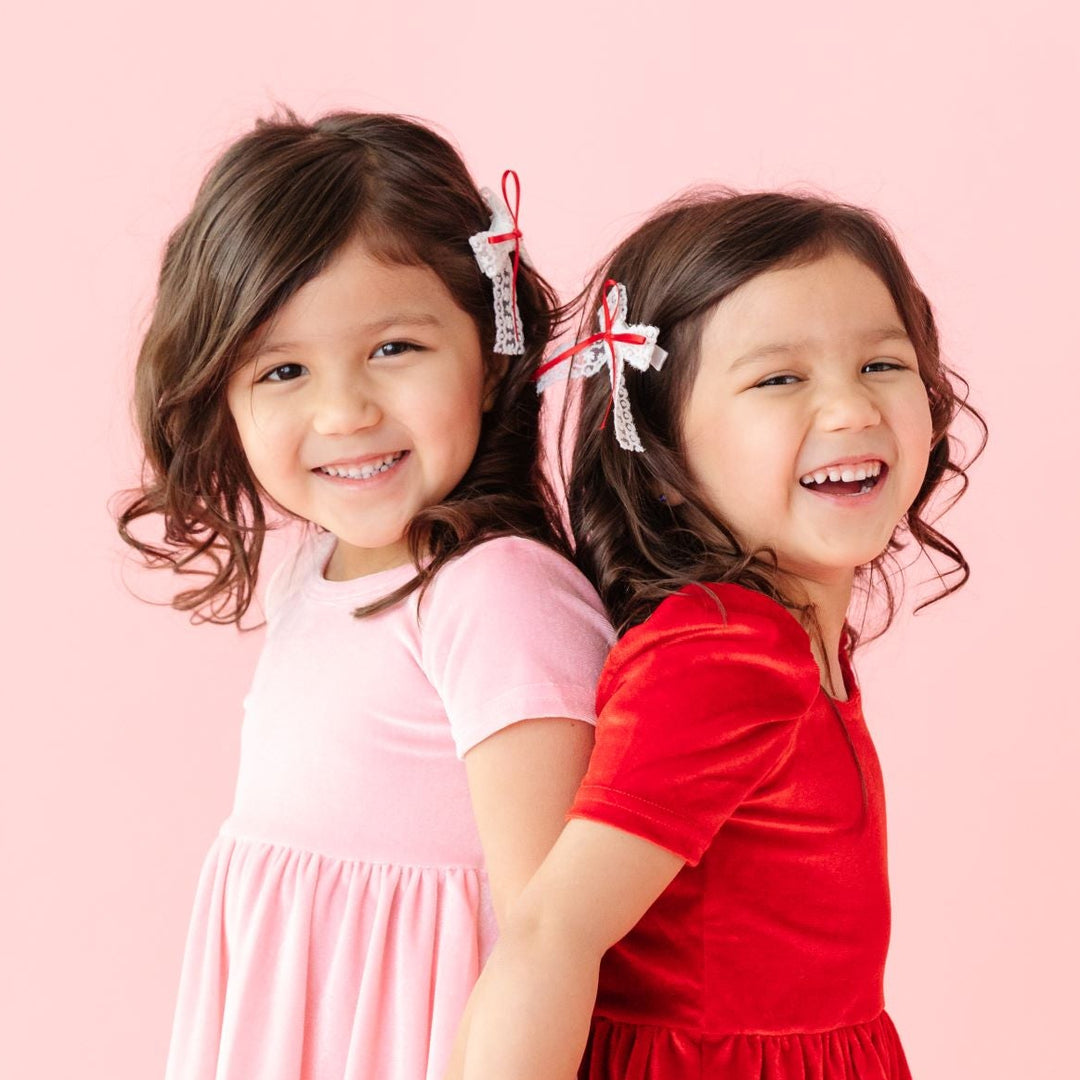 little girls in coordinating pink and red velvet dresses and matching white lace and red ribbon pigtail bows 